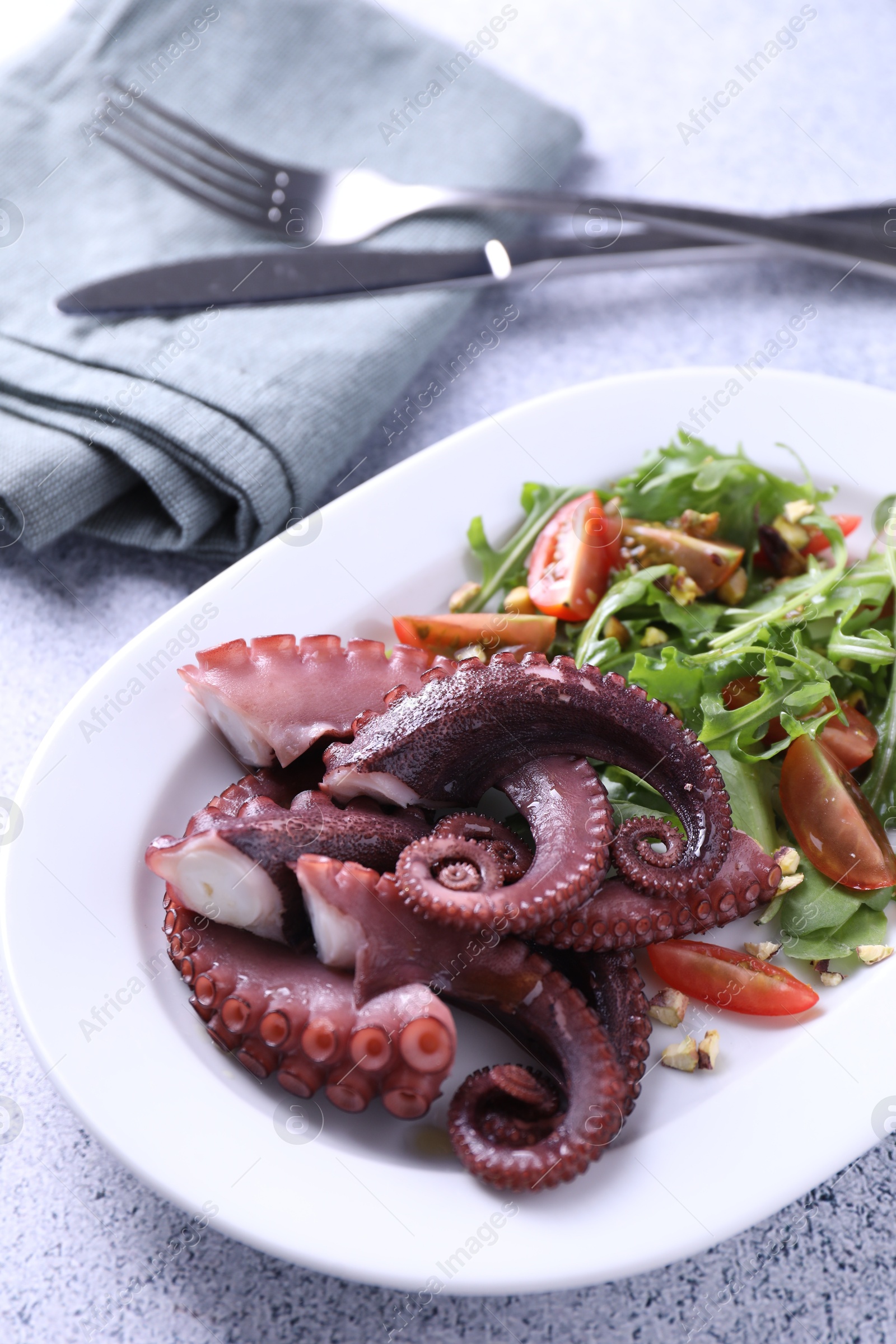 Photo of Plate with tasty boiled octopus tentacles and salad on grey textured table, above view