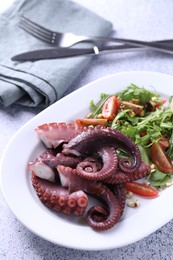 Photo of Plate with tasty boiled octopus tentacles and salad on grey textured table, above view