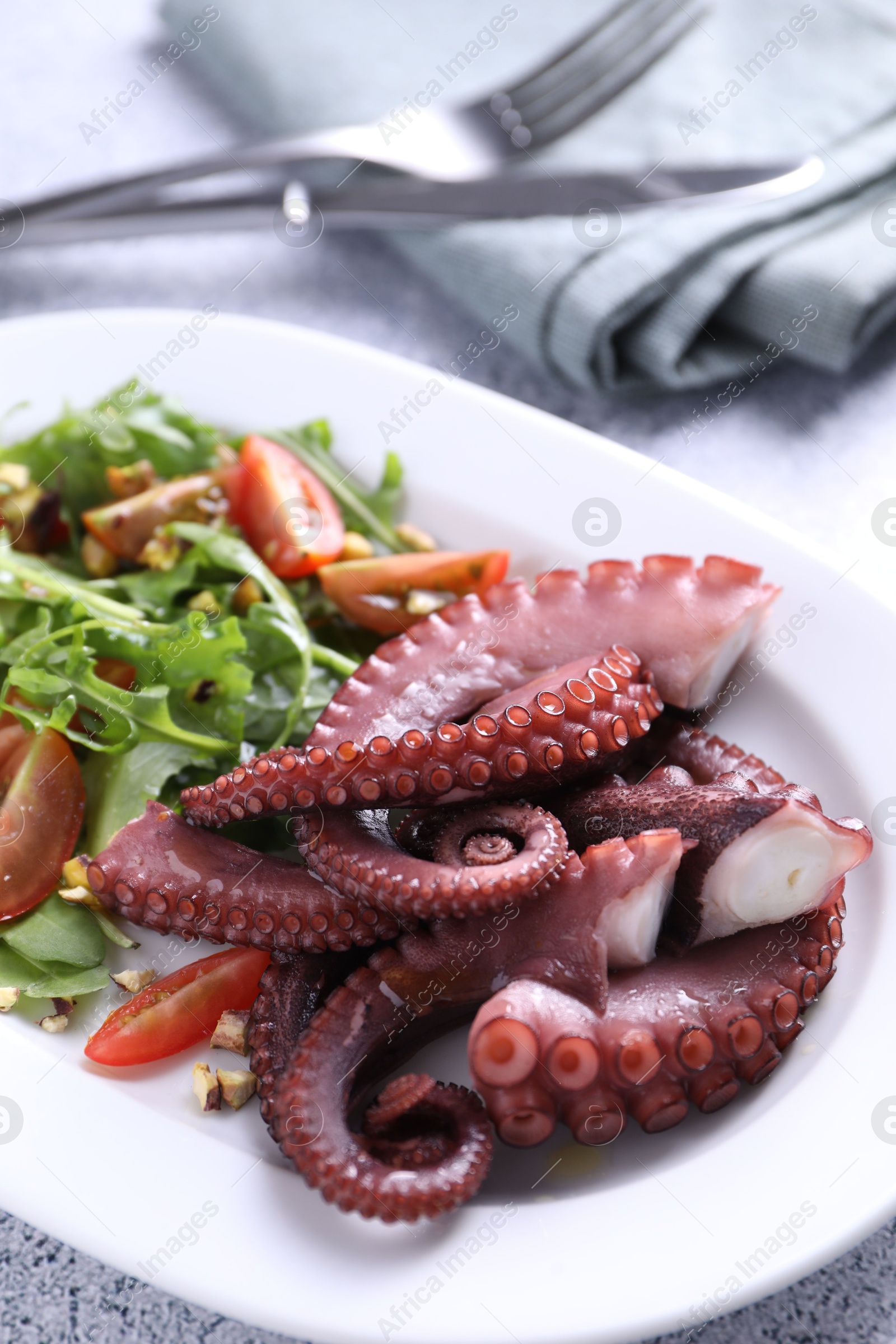 Photo of Plate with tasty boiled octopus tentacles and salad on grey textured table, above view