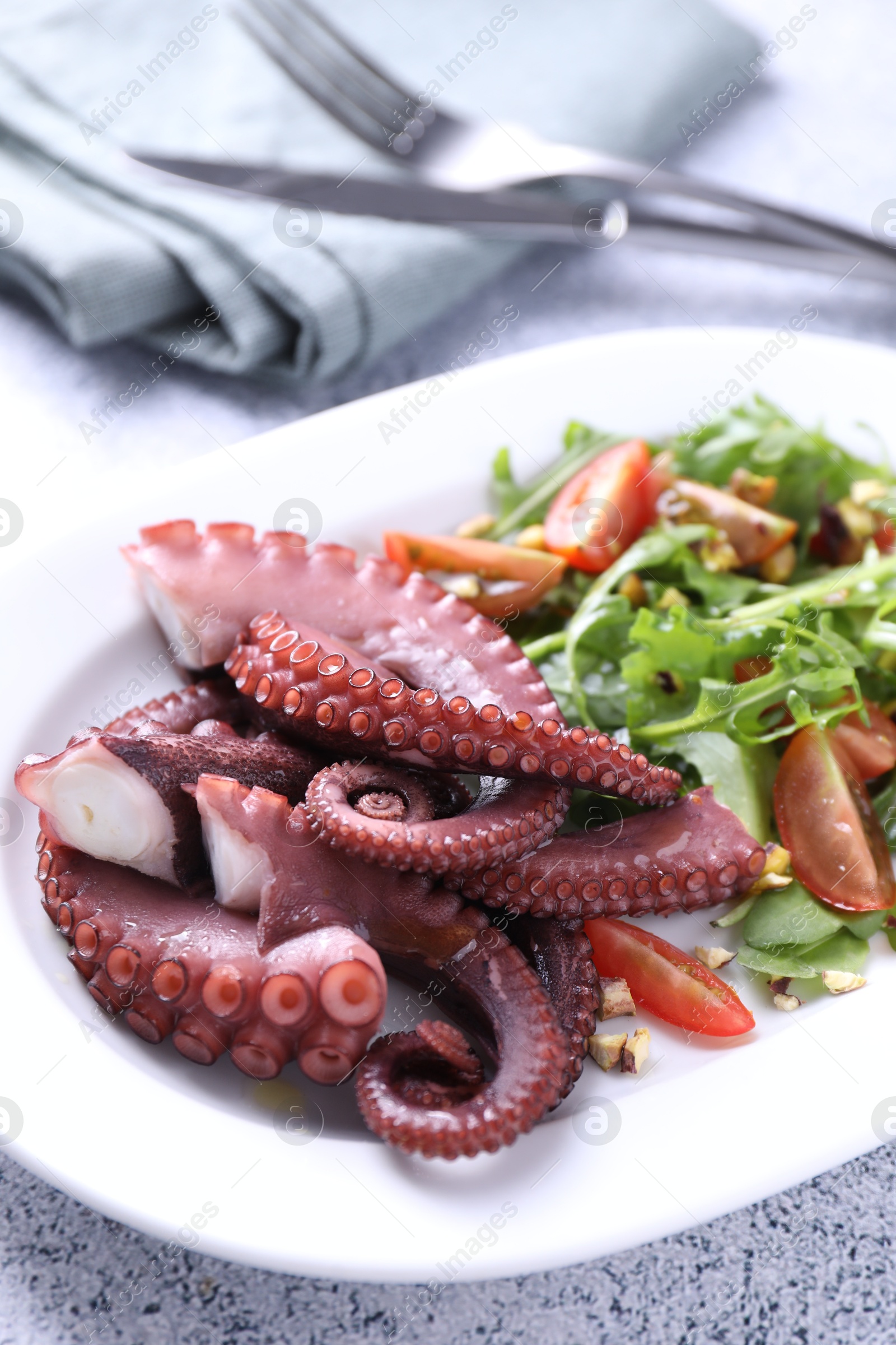 Photo of Plate with tasty boiled octopus tentacles and salad on grey textured table, above view