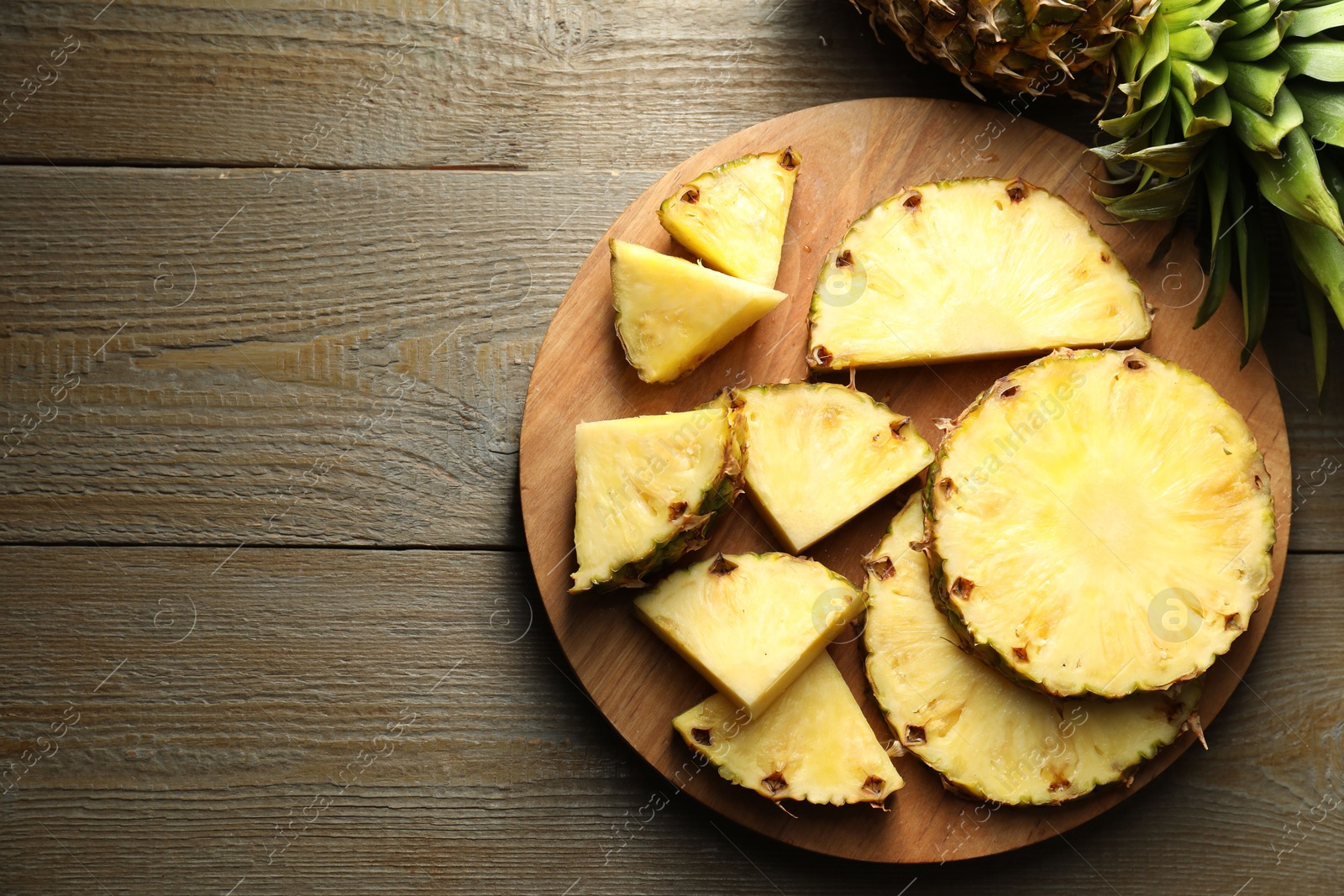 Photo of Slices of ripe pineapple on wooden table, top view. Space for text