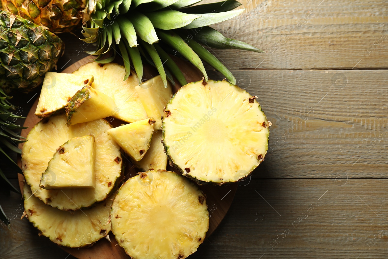 Photo of Cut ripe pineapples on wooden table, top view. Space for text