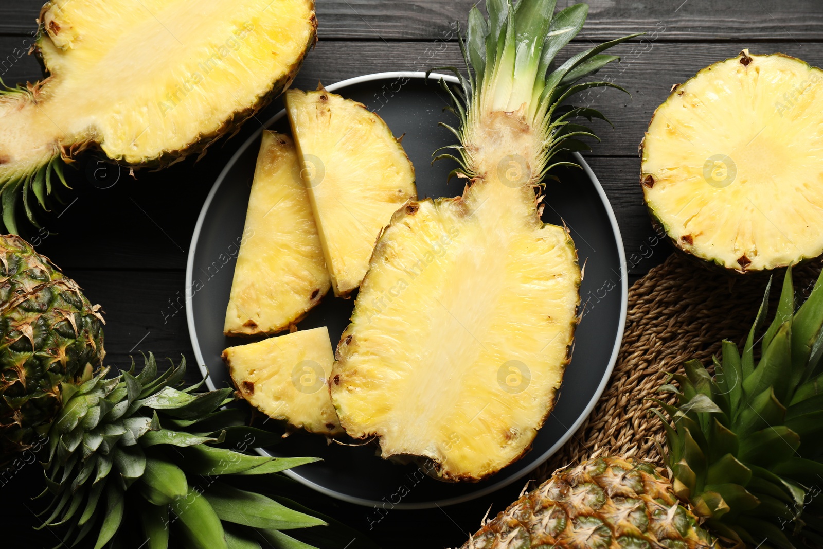 Photo of Fresh ripe pineapples on black wooden table, top view