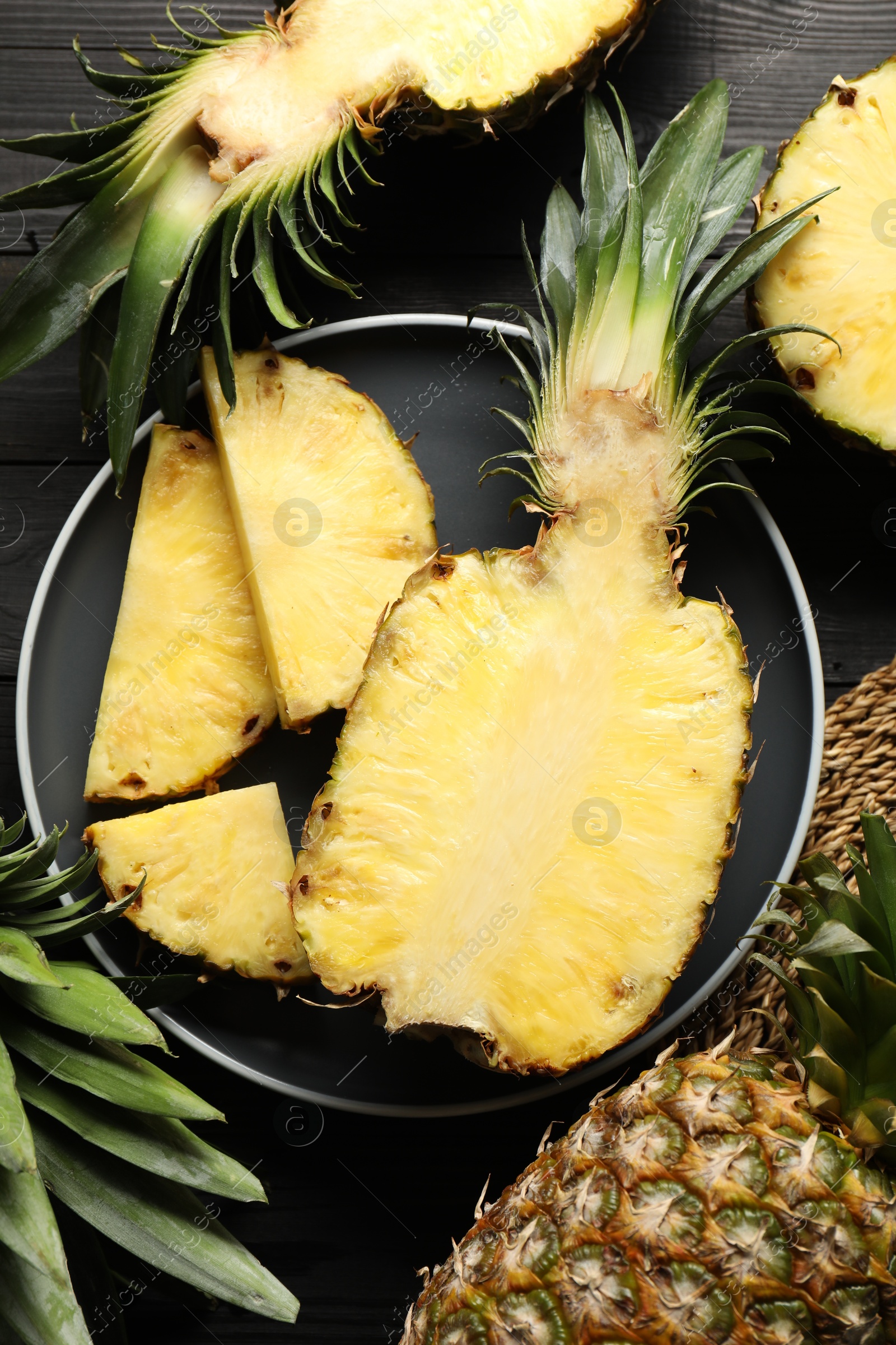 Photo of Fresh ripe pineapples on black wooden table, top view