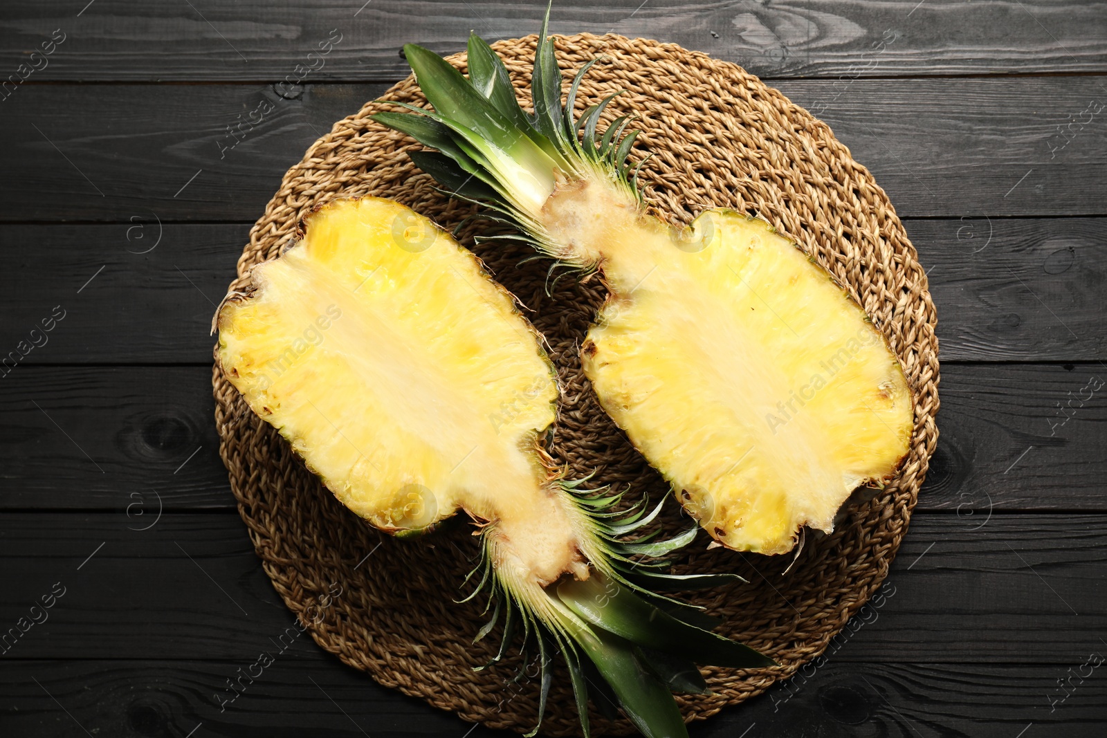 Photo of Halves of ripe pineapple on black wooden table, top view