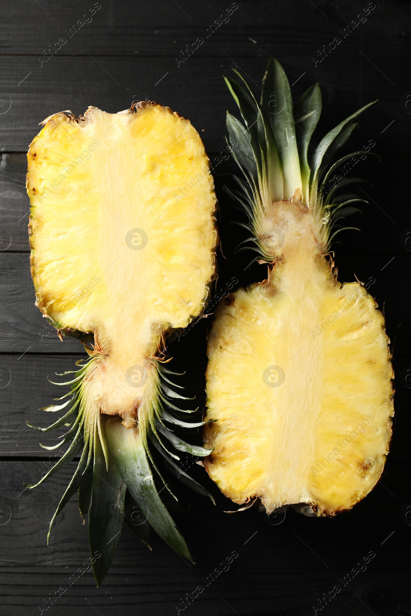 Photo of Halves of ripe pineapple on black wooden table, top view