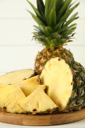 Photo of Whole and sliced fresh ripe pineapples on white table, closeup