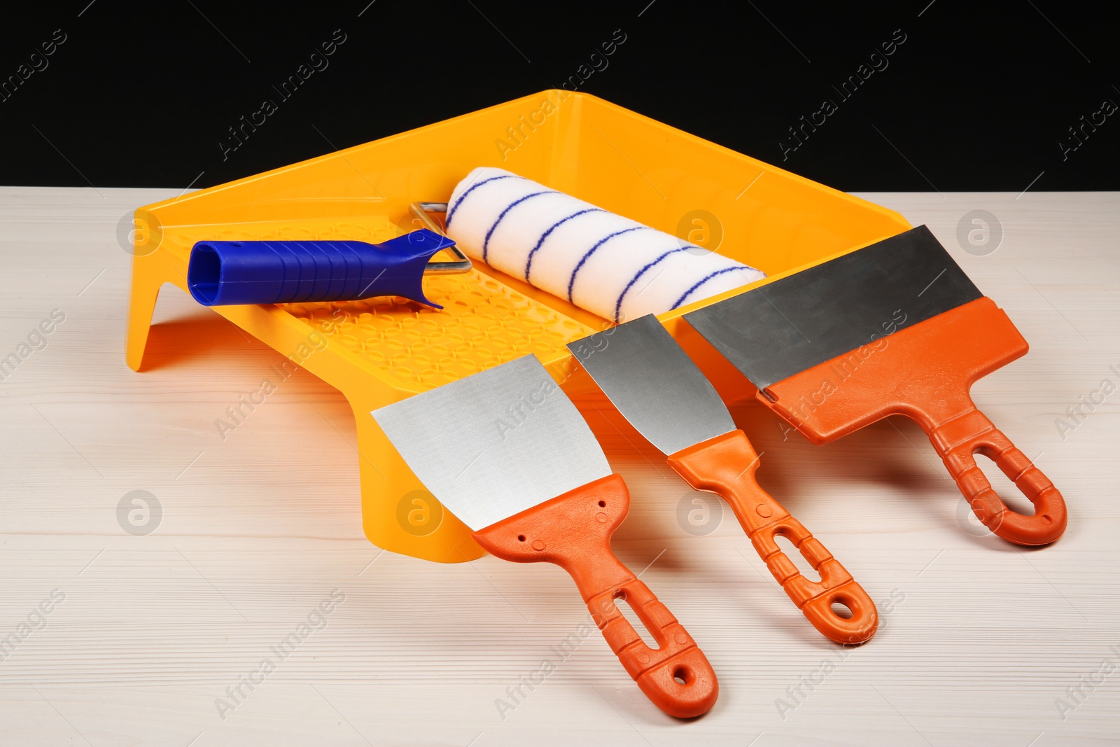 Photo of Paint roller, tray and putty knives on light wooden table. Construction tools