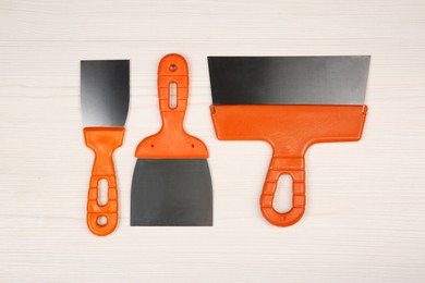 Photo of Putty knives on light wooden table, flat lay. Construction tools