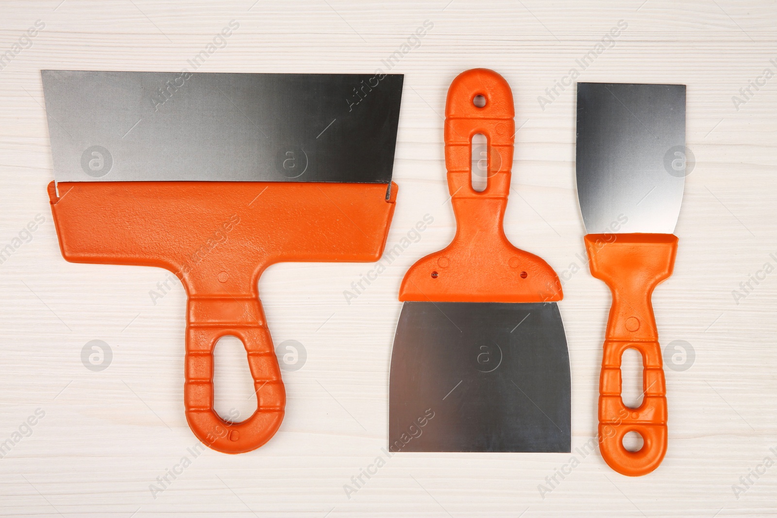 Photo of Putty knives on light wooden table, flat lay. Construction tools