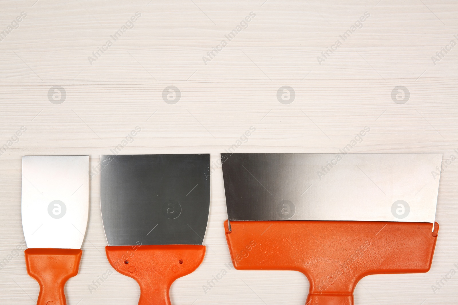 Photo of Putty knives on light wooden table, flat lay with space for text. Construction tools