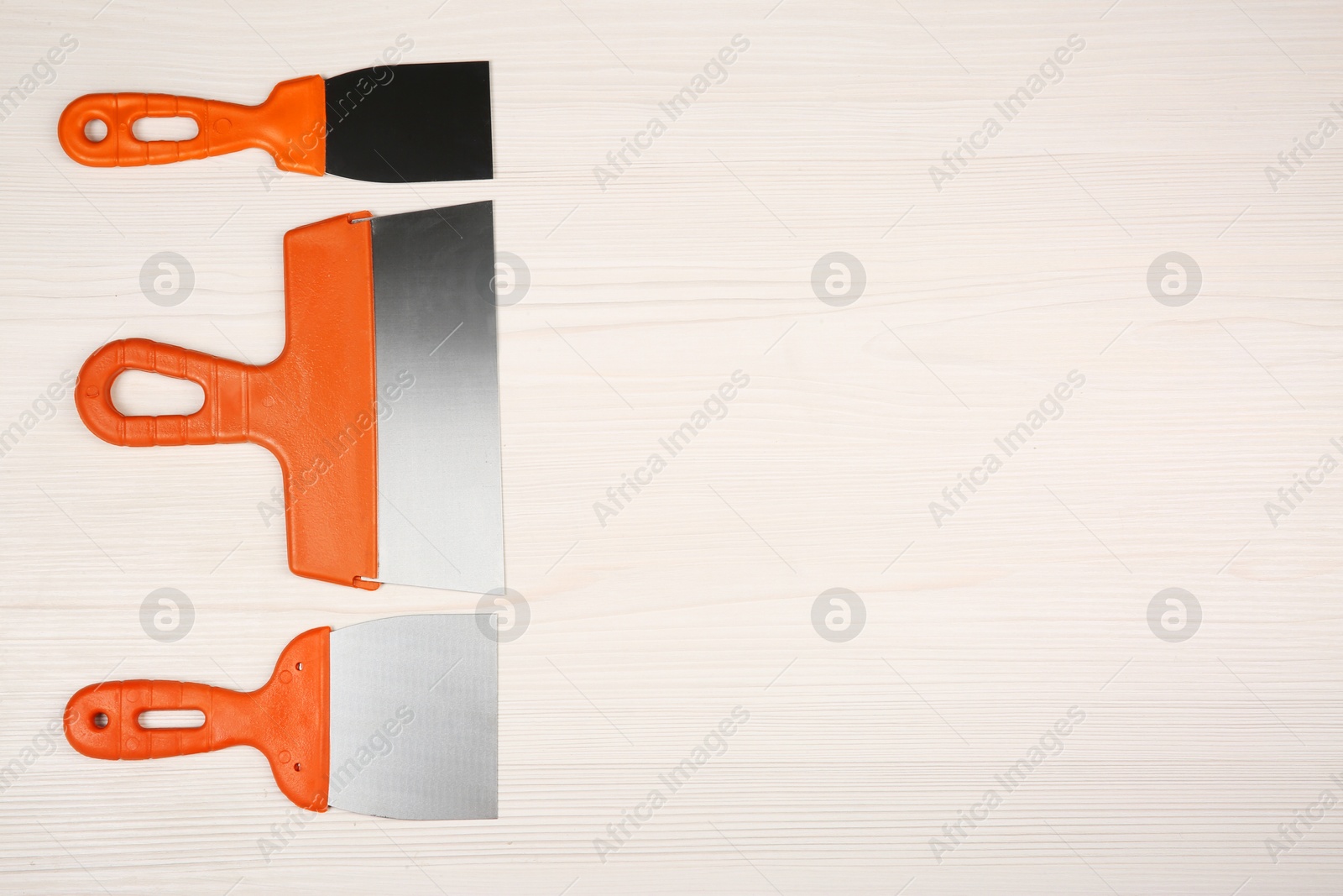 Photo of Putty knives on light wooden table, flat lay with space for text. Construction tools