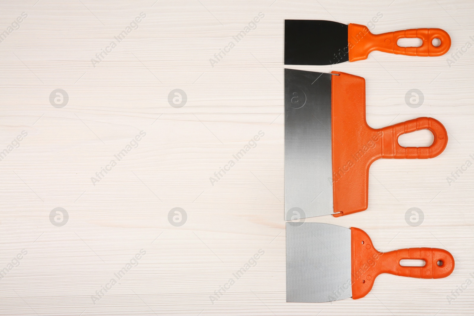 Photo of Putty knives on light wooden table, flat lay with space for text. Construction tools