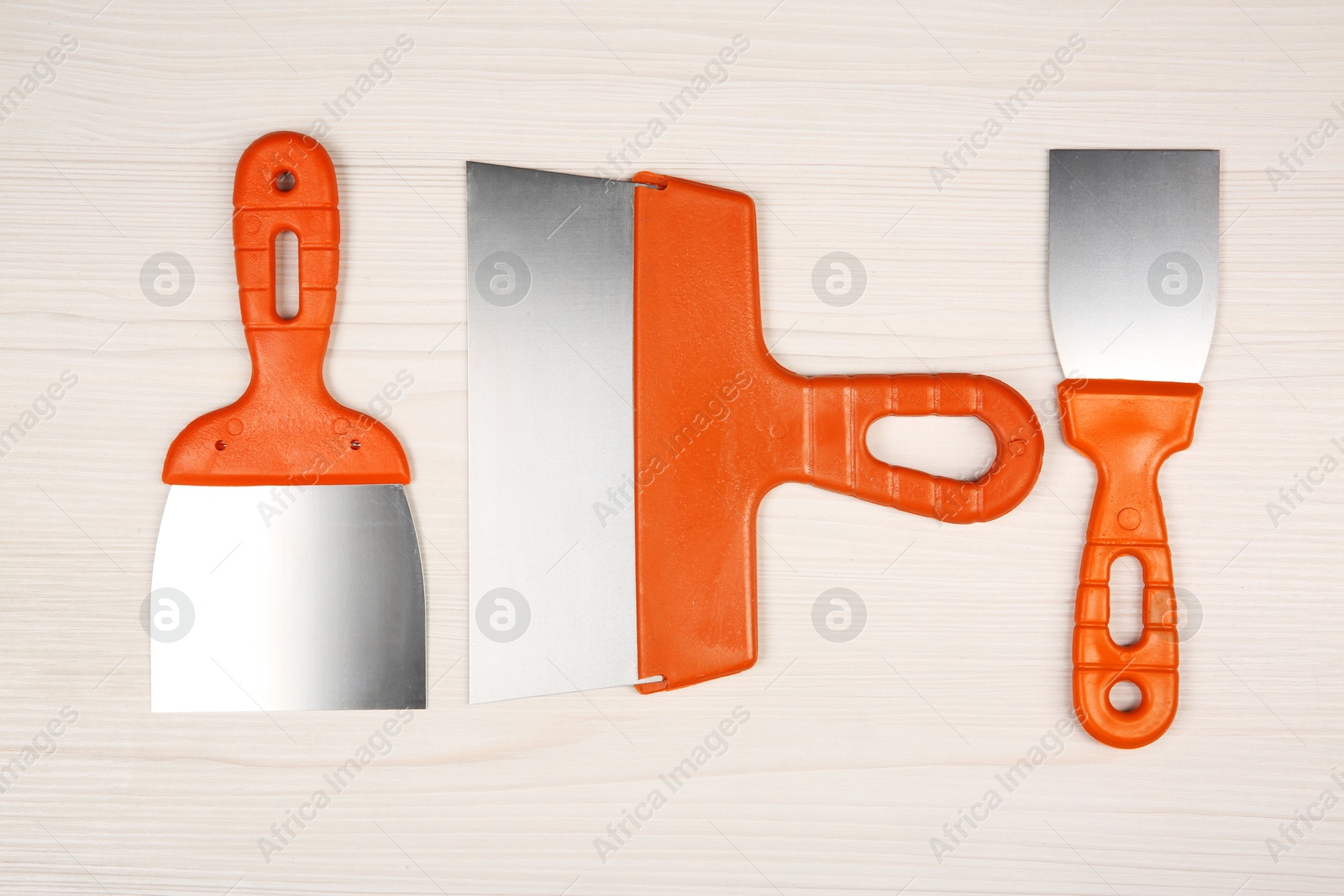 Photo of Putty knives on light wooden table, flat lay. Construction tools