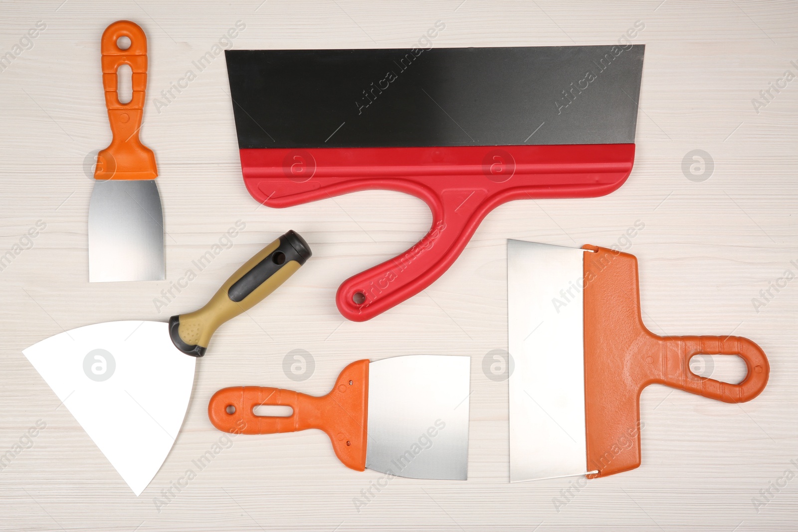 Photo of Putty knives on light wooden table, flat lay. Construction tools