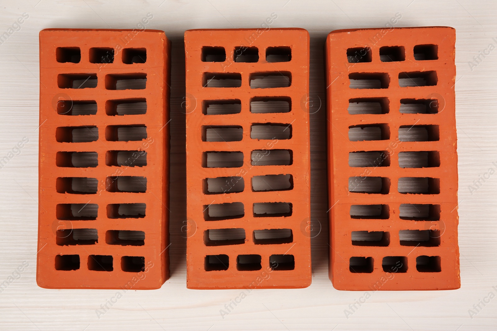 Photo of Many red bricks on light wooden table, flat lay. Building material