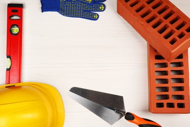 Photo of Red bricks, different construction tools and safety equipment on light wooden table, flat lay. Space for text