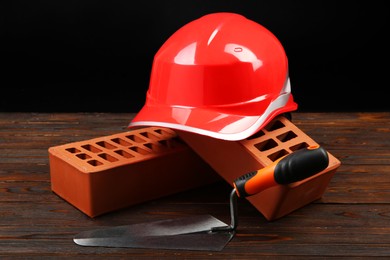 Photo of Red bricks, putty knife and hard hat on wooden table. Building material