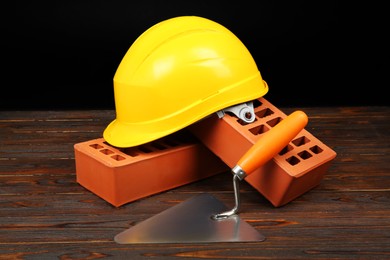 Red bricks, putty knife and yellow hard hat on wooden table. Building material