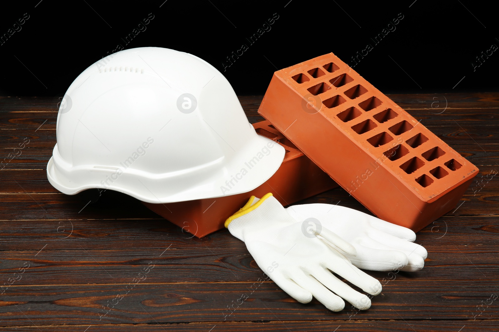 Photo of Red bricks, white hard hat and rubber gloves on wooden table. Building material