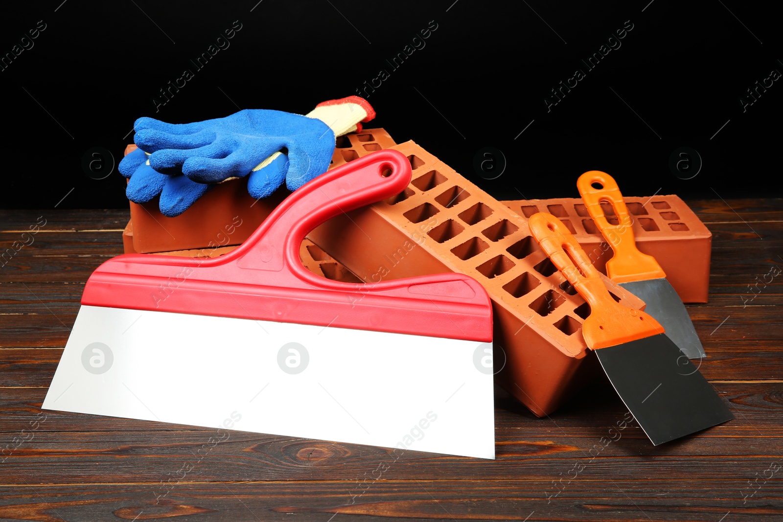 Photo of Red bricks, putty knives and rubber gloves on wooden table. Building material and construction tools