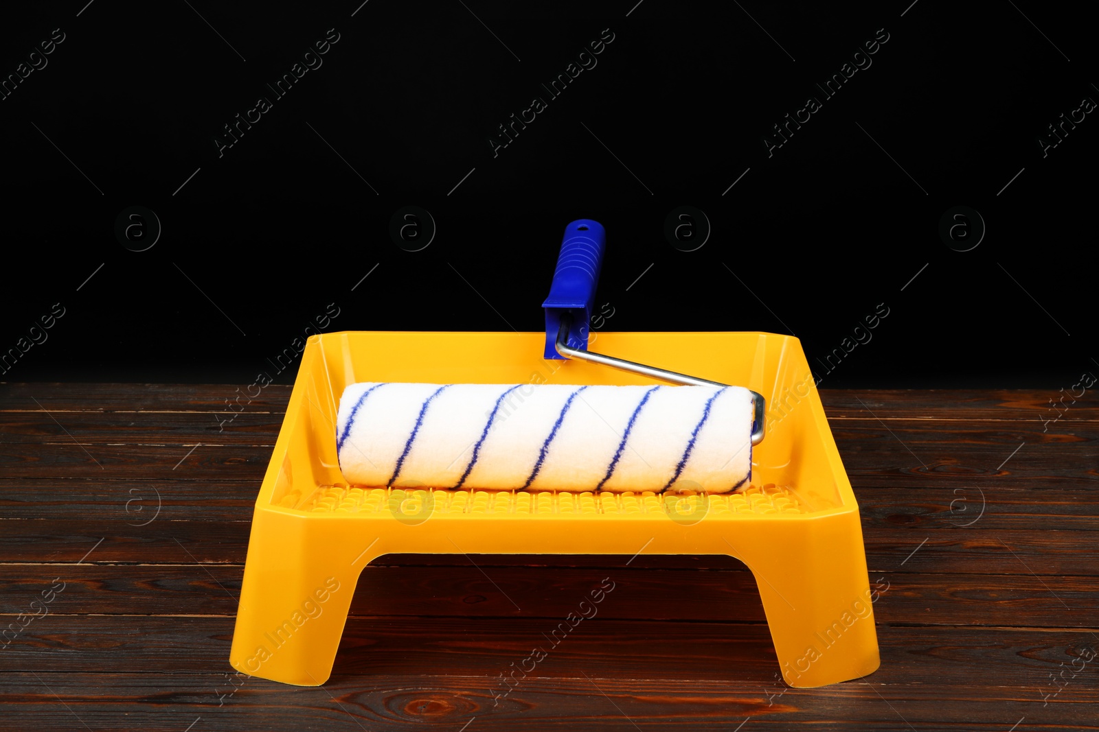 Photo of Tray and paint roller on wooden table. Construction tools