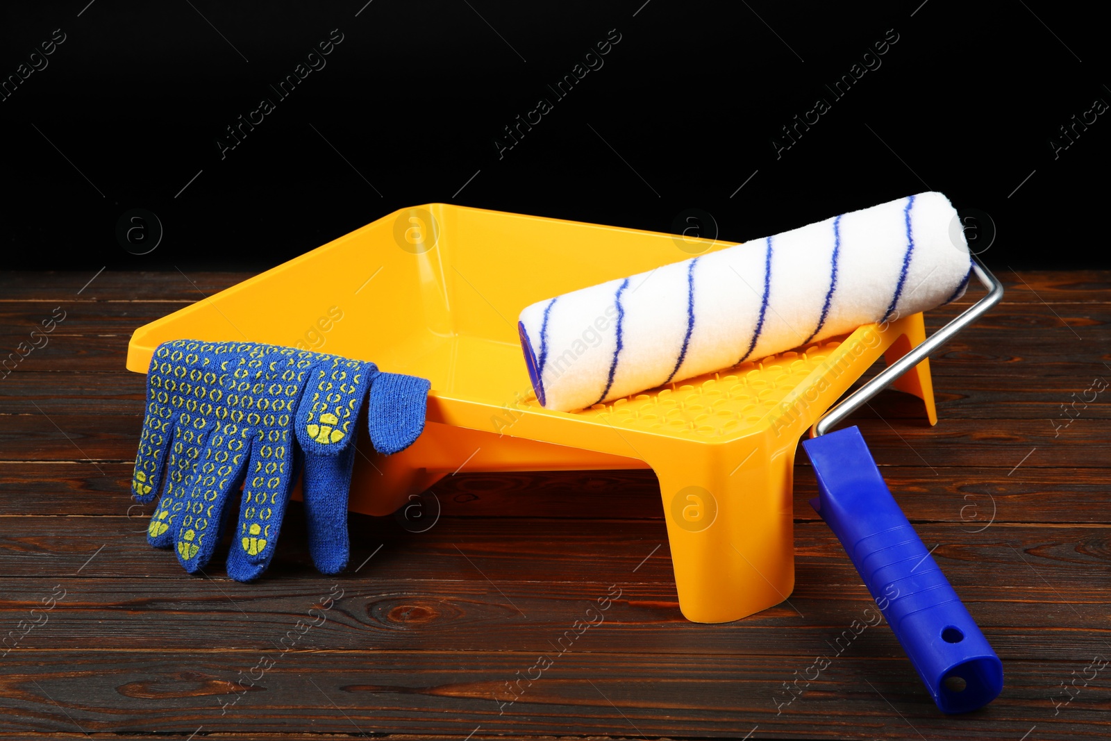 Photo of Tray, paint roller and rubber gloves on wooden table. Building material and construction tools