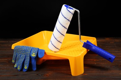 Photo of Tray, paint roller and rubber gloves on wooden table. Building material and construction tools