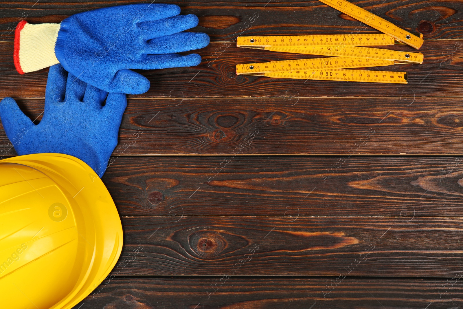 Photo of Yellow hard hat, rubber gloves and folding ruler on wooden table, flat lay. Space for text