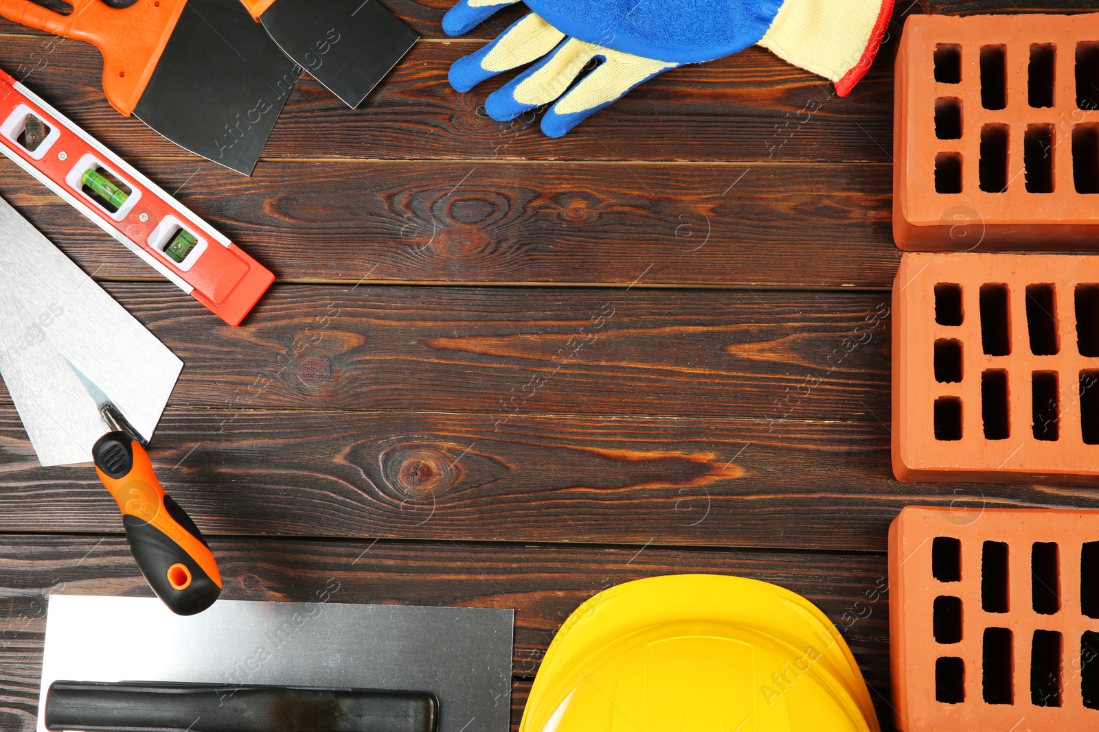 Photo of Red bricks, different construction tools and safety equipment on wooden table, flat lay. Space for text