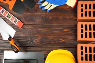 Photo of Red bricks, different construction tools and safety equipment on wooden table, flat lay. Space for text