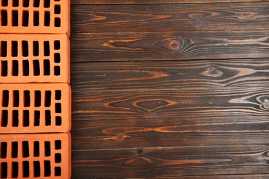 Many red bricks on wooden table, flat lay with space for text. Building material