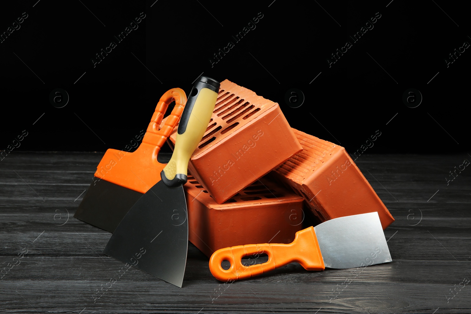 Photo of Red bricks and putty knives on wooden table. Building material and construction tools