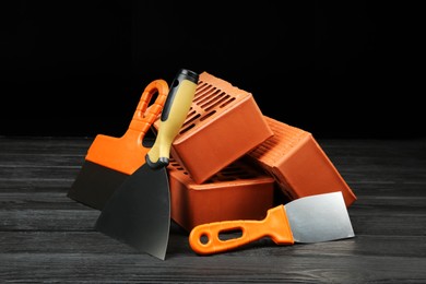 Photo of Red bricks and putty knives on wooden table. Building material and construction tools