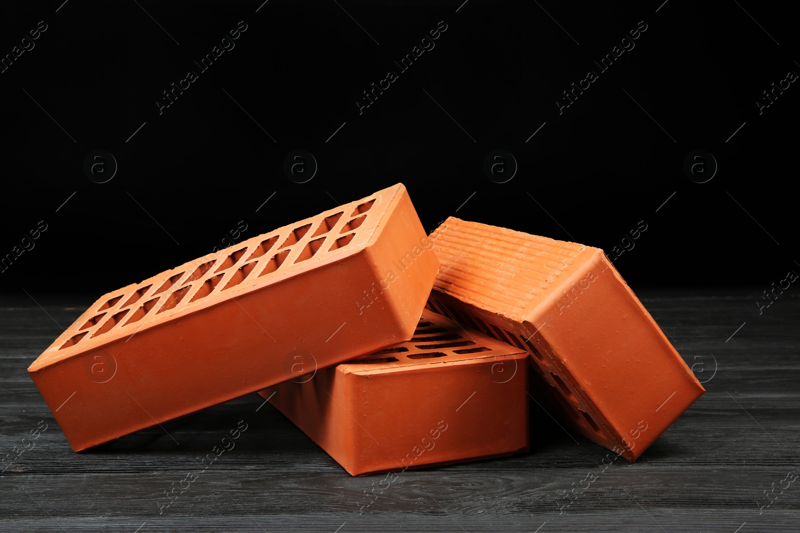 Photo of Many red bricks on dark wooden table. Building material