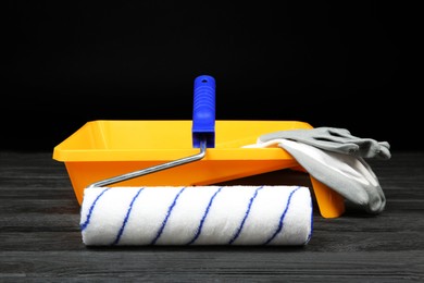 Photo of Tray, paint roller and rubber gloves on dark wooden table