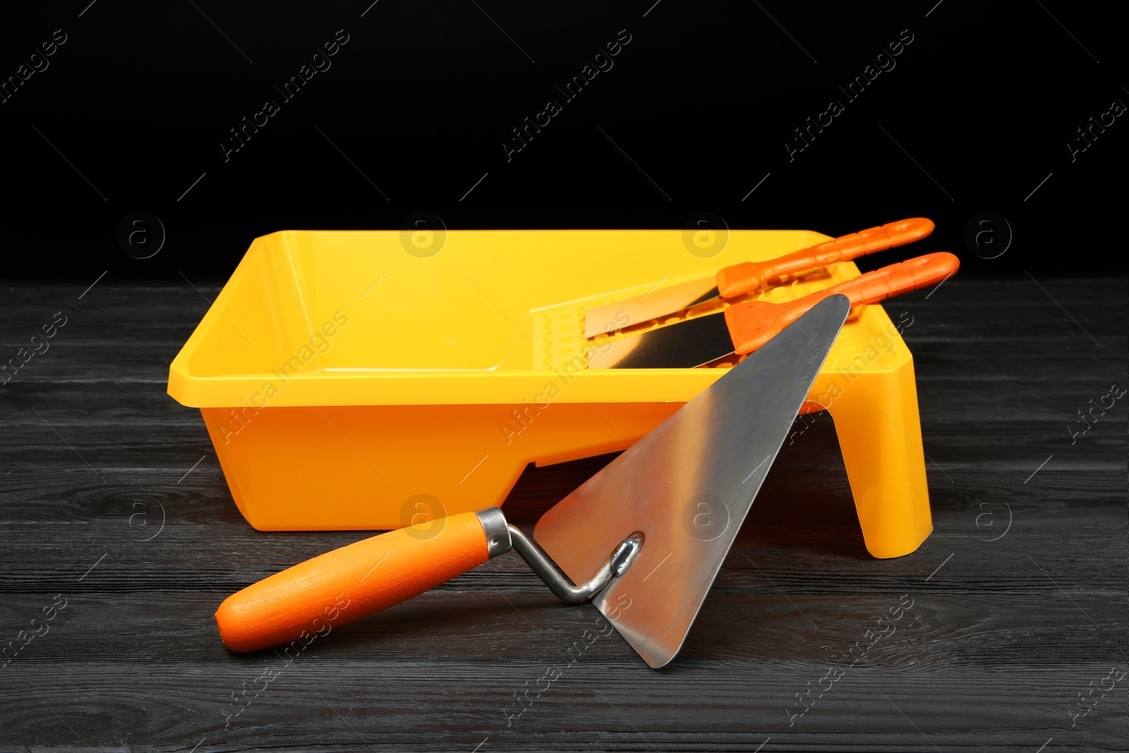 Photo of Tray and putty knives on dark wooden table. Construction tools