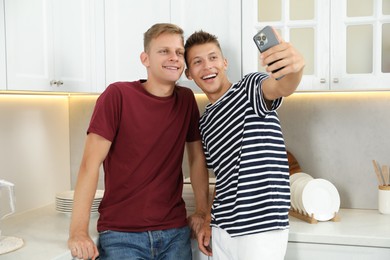 Two happy brothers taking selfie in kitchen