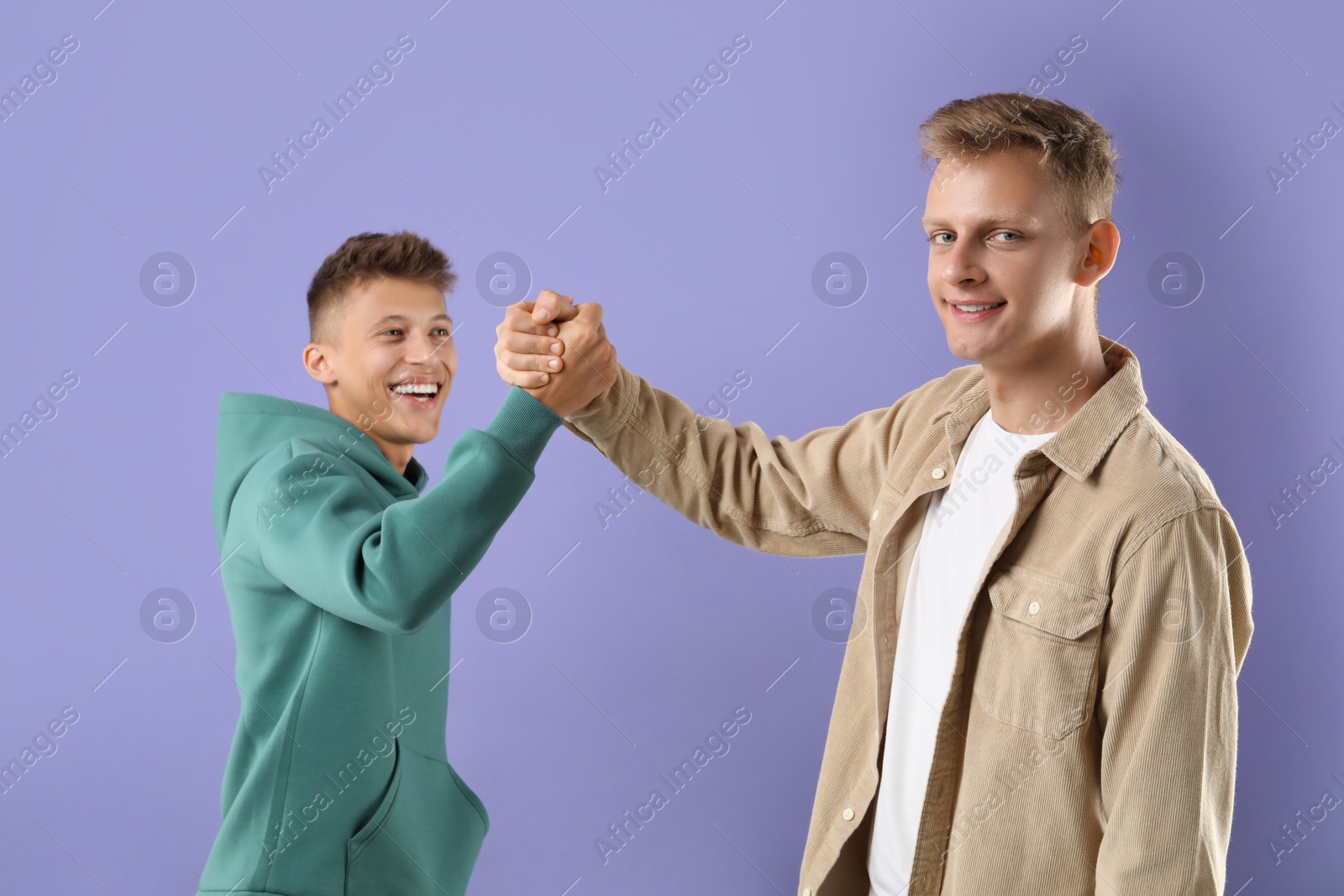 Photo of Happy brothers clasping hands on violet background