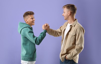 Photo of Happy brothers clasping hands on violet background