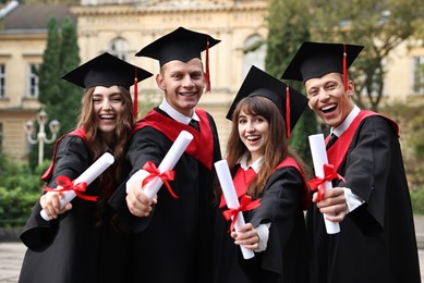 Photo of Happy students with diplomas after graduation ceremony outdoors