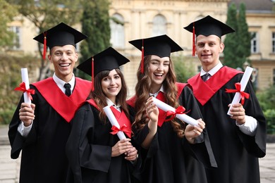 Photo of Happy students with diplomas after graduation ceremony outdoors