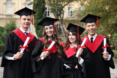 Photo of Happy students with diplomas after graduation ceremony outdoors