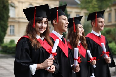 Photo of Happy students with diplomas after graduation ceremony outdoors, selective focus