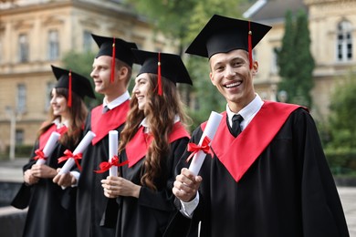 Happy students with diplomas after graduation ceremony outdoors, selective focus