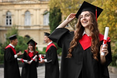 Photo of Happy students with diplomas after graduation ceremony outdoors, selective focus