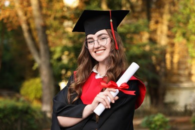 Photo of Happy student with diploma after graduation ceremony outdoors