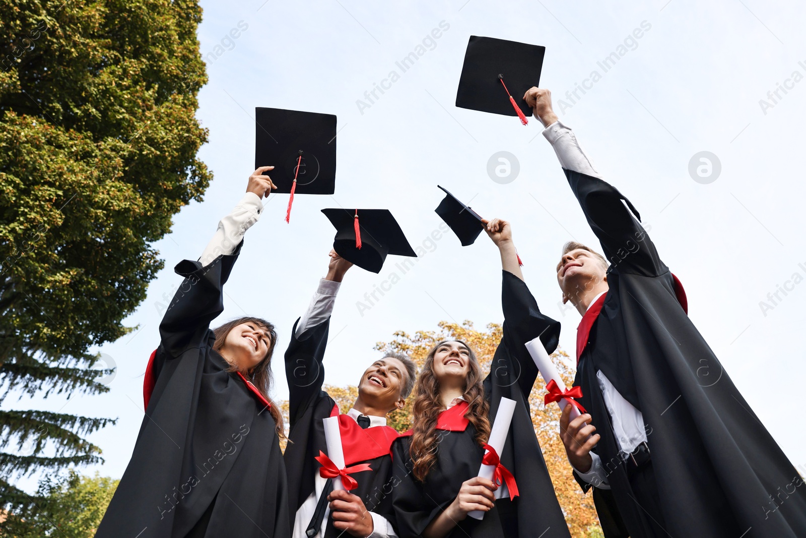 Photo of Graduation ceremony. Group of students with diplomas throwing hats outdoors, low angle view