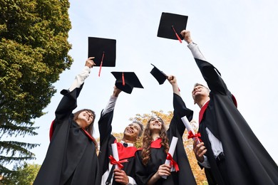 Graduation ceremony. Group of students with diplomas throwing hats outdoors, low angle view