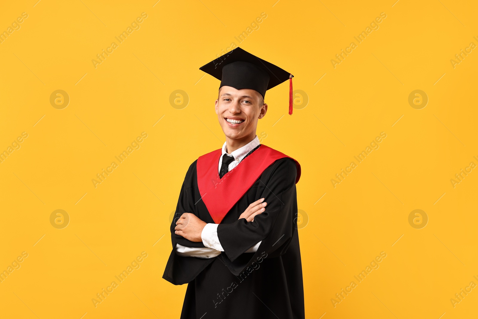 Photo of Happy student with crossed arms after graduation on orange background